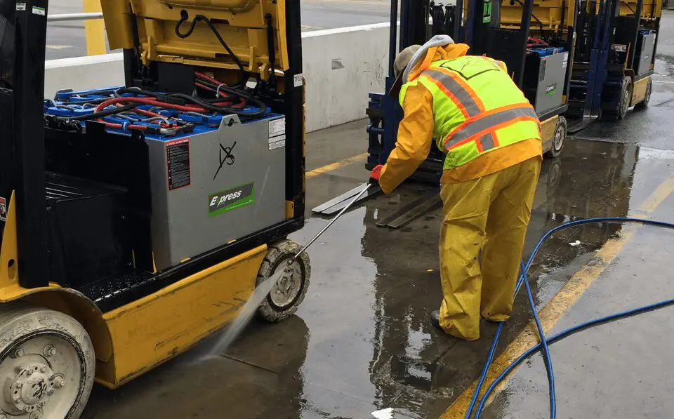 Worker cleaning forklift with water